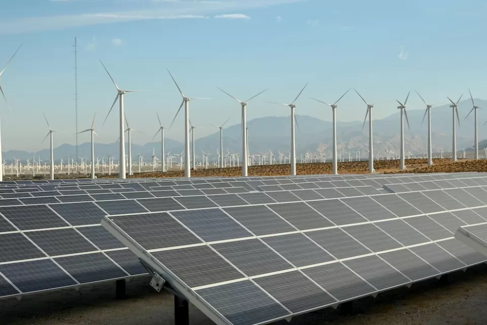 Large solar panel installation and wind turbines with Southern California desert mountains in background.